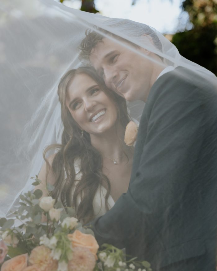 Bride and groom smiling beneath her veil